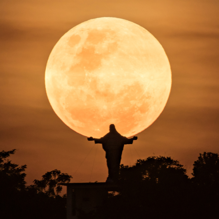 Christusstatue vor einem großen, leuchtenden Vollmond bei Sonnenuntergang.